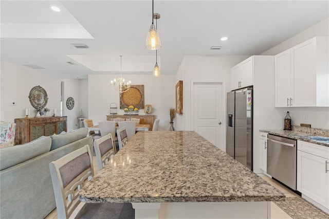 kitchen with a tray ceiling, a kitchen island, a breakfast bar, white cabinets, and appliances with stainless steel finishes