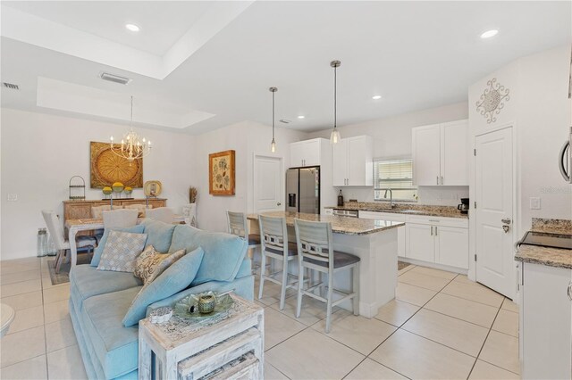 kitchen with light stone countertops, a kitchen island, stainless steel appliances, a tray ceiling, and decorative light fixtures