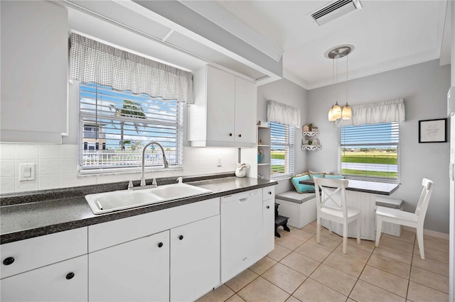 kitchen featuring white dishwasher, sink, light tile patterned floors, decorative light fixtures, and white cabinetry