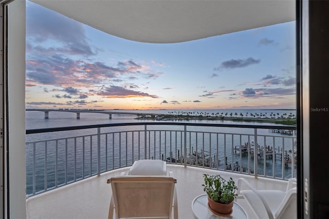 balcony at dusk featuring a water view