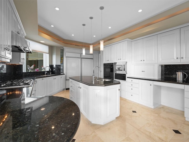 kitchen with decorative backsplash, extractor fan, sink, pendant lighting, and a center island with sink