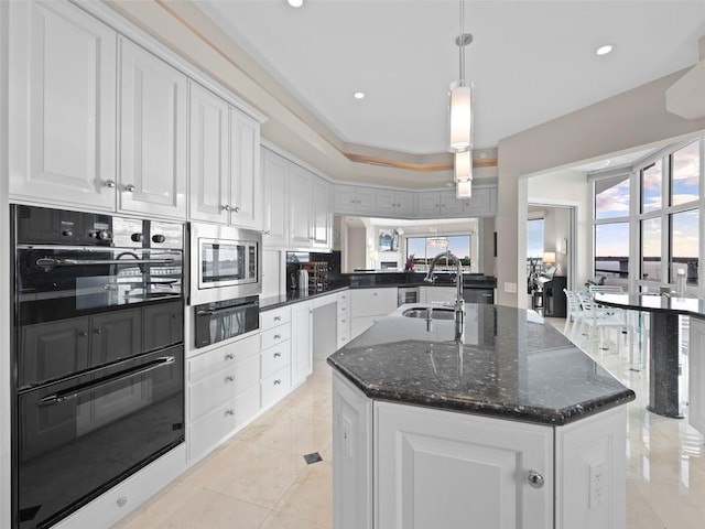 kitchen with white cabinets, black double oven, a center island with sink, and sink