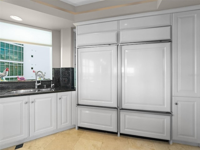 kitchen with white cabinets, light tile patterned floors, sink, and dark stone counters