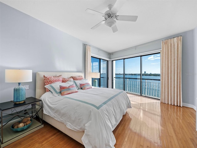 bedroom with hardwood / wood-style floors, a water view, ceiling fan, and access to outside