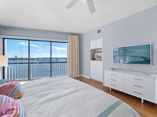 bedroom featuring access to outside, dark hardwood / wood-style flooring, a water view, and ceiling fan