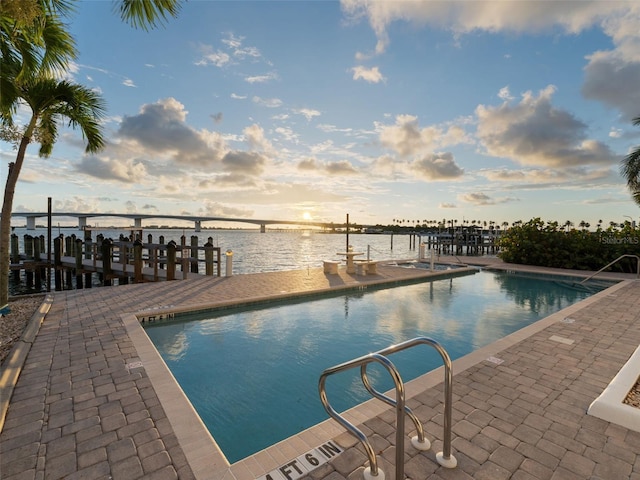 view of swimming pool featuring a patio area, a water view, and a dock