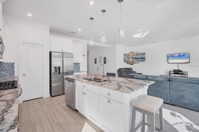 kitchen with sink, decorative light fixtures, a kitchen island with sink, white cabinets, and appliances with stainless steel finishes