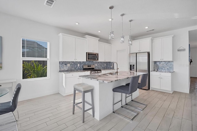 kitchen featuring appliances with stainless steel finishes, a kitchen breakfast bar, light stone counters, a kitchen island with sink, and white cabinets