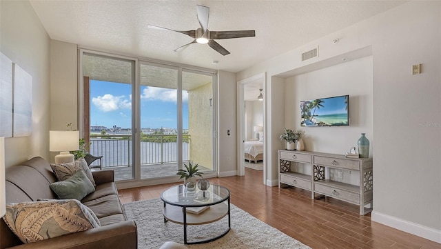 living room with a wealth of natural light, ceiling fan, a textured ceiling, and a wall of windows