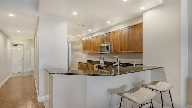 kitchen with kitchen peninsula, appliances with stainless steel finishes, a kitchen bar, sink, and dark stone countertops