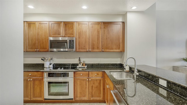 kitchen with appliances with stainless steel finishes, dark stone counters, and sink