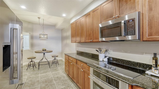 kitchen featuring light tile patterned flooring, stainless steel appliances, hanging light fixtures, and dark stone countertops