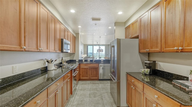 kitchen with sink, dark stone countertops, light tile patterned floors, a textured ceiling, and appliances with stainless steel finishes