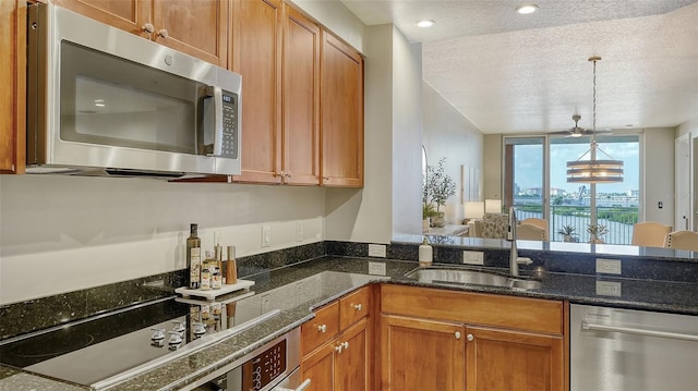 kitchen with sink, hanging light fixtures, dark stone countertops, a textured ceiling, and appliances with stainless steel finishes