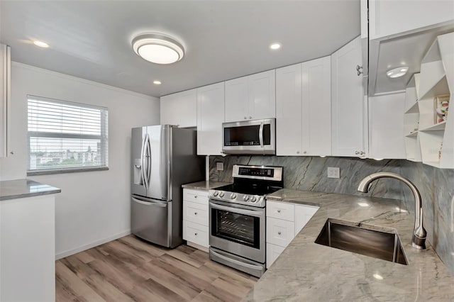 kitchen featuring stainless steel appliances, ornamental molding, light stone counters, sink, and white cabinetry