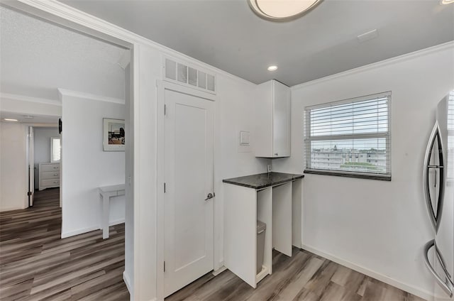 kitchen with hardwood / wood-style flooring, stainless steel fridge, ornamental molding, and white cabinetry