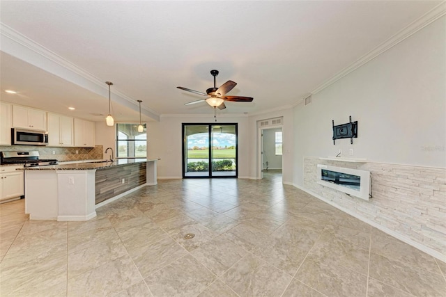 kitchen with white cabinets, appliances with stainless steel finishes, decorative light fixtures, dark stone counters, and an island with sink