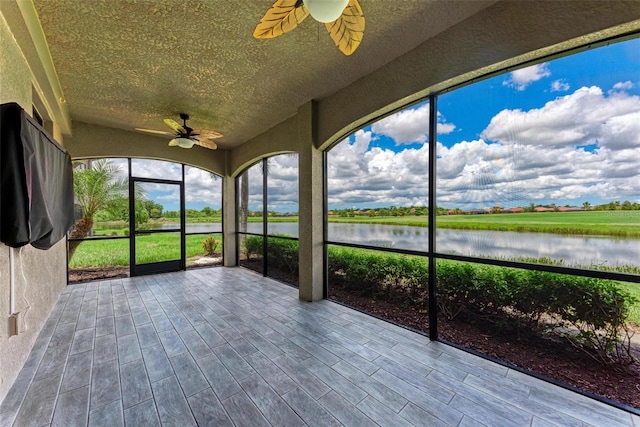 unfurnished sunroom with ceiling fan and a water view