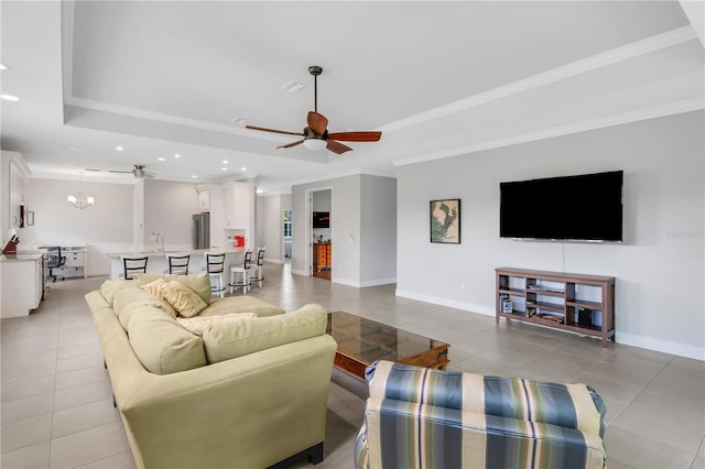 tiled living room with sink, crown molding, ceiling fan with notable chandelier, and a raised ceiling