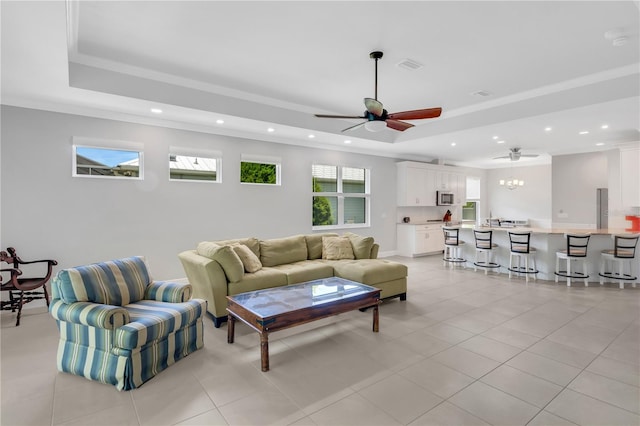 living room with ceiling fan, a tray ceiling, ornamental molding, and light tile patterned floors