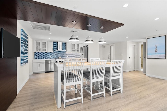 kitchen with wall chimney exhaust hood, hanging light fixtures, stainless steel appliances, decorative backsplash, and white cabinets