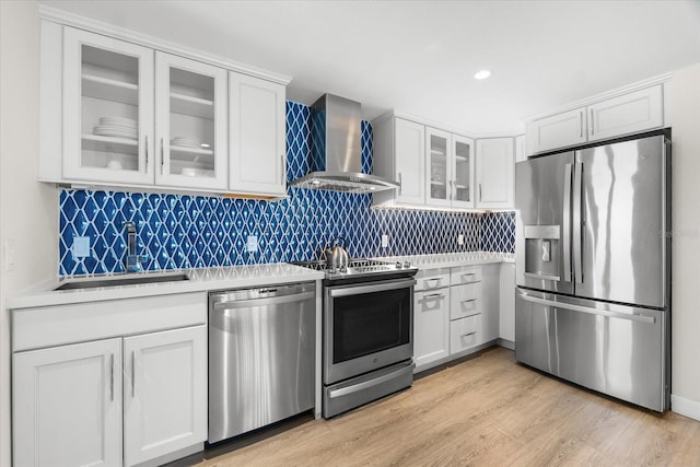 kitchen with sink, wall chimney exhaust hood, stainless steel appliances, light hardwood / wood-style floors, and white cabinets