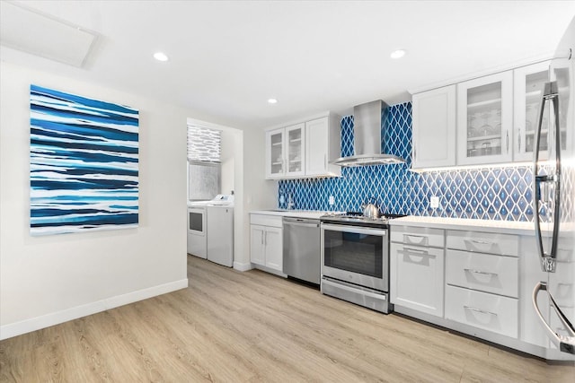 kitchen with appliances with stainless steel finishes, separate washer and dryer, white cabinets, light hardwood / wood-style floors, and wall chimney exhaust hood