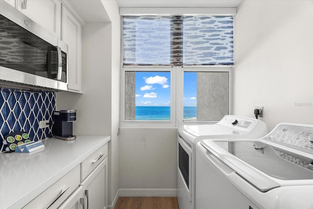 washroom with washing machine and clothes dryer, a water view, cabinets, and hardwood / wood-style flooring