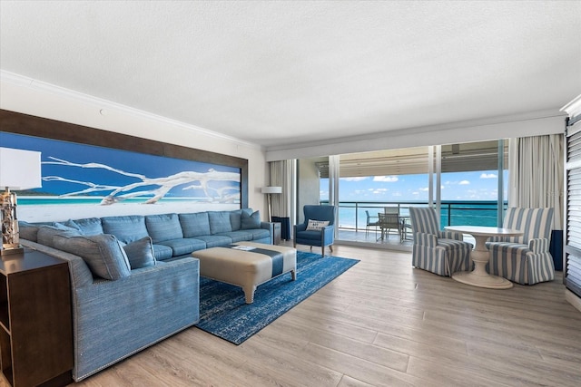 living room with a textured ceiling, light wood-type flooring, a water view, and ornamental molding