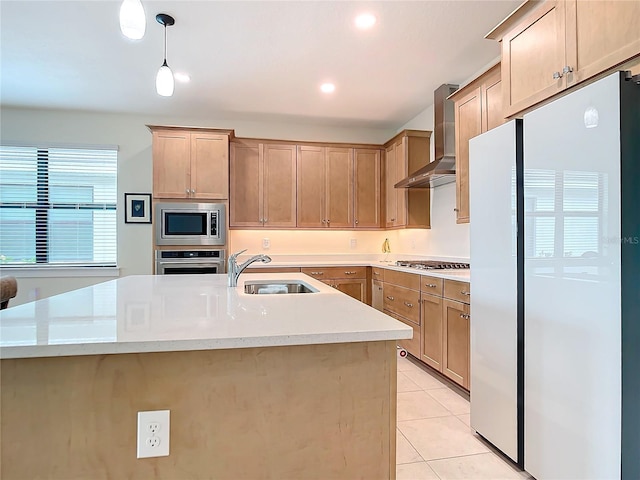 kitchen featuring sink, hanging light fixtures, wall chimney range hood, a kitchen island with sink, and appliances with stainless steel finishes