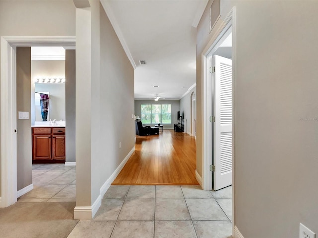 hall with sink, light tile patterned floors, and crown molding