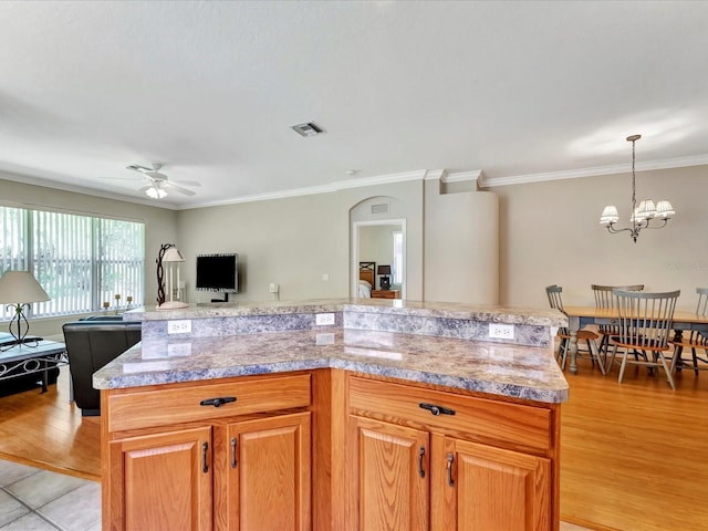 kitchen with ceiling fan with notable chandelier, a center island, hanging light fixtures, light wood-type flooring, and crown molding