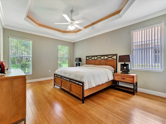 bedroom featuring a raised ceiling, ceiling fan, multiple windows, and ornamental molding