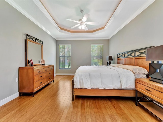 bedroom with light wood-type flooring, ceiling fan, ornamental molding, and a raised ceiling