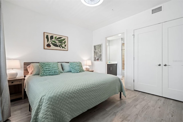 bedroom featuring light wood finished floors, visible vents, ensuite bath, and a closet