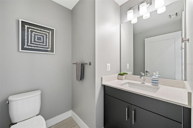 half bath with visible vents, baseboards, toilet, wood finished floors, and vanity