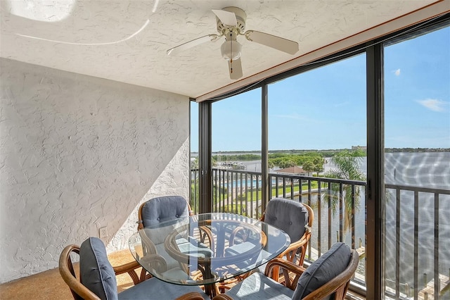 sunroom with ceiling fan and a water view