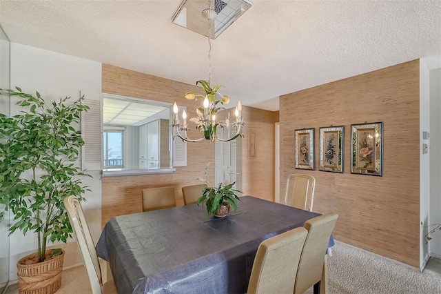 dining space with light colored carpet, a textured ceiling, an inviting chandelier, and wood walls