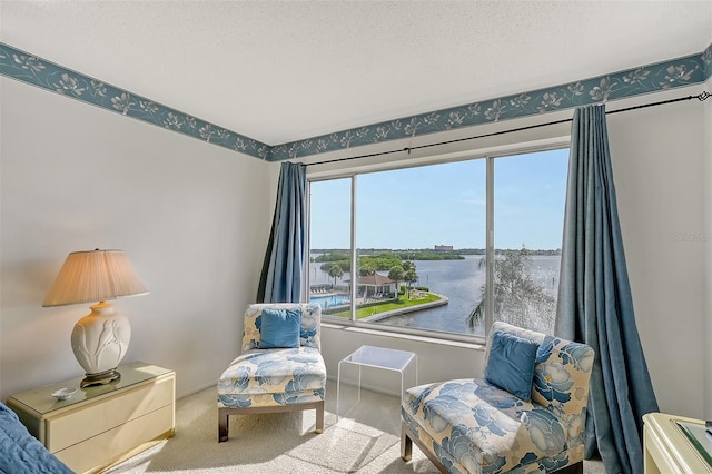 sitting room featuring a water view, light colored carpet, a textured ceiling, and a wealth of natural light