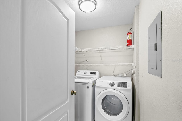 laundry room featuring electric panel, washing machine and dryer, and a textured ceiling