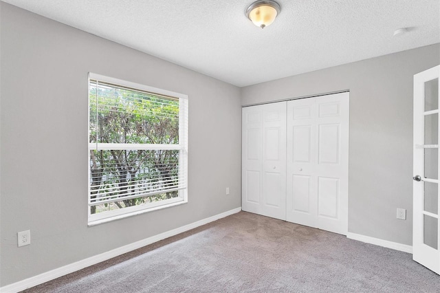 unfurnished bedroom featuring carpet flooring, multiple windows, a closet, and a textured ceiling