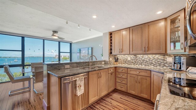 kitchen featuring light stone counters, ceiling fan, sink, a water view, and dishwasher