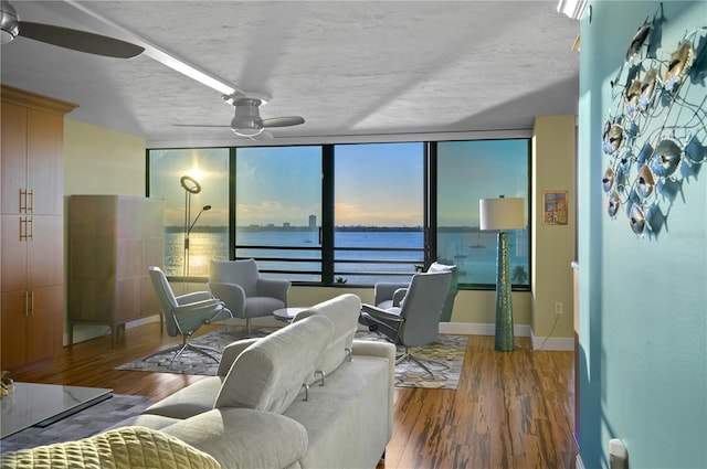 living room featuring ceiling fan, hardwood / wood-style floors, a water view, and a wall of windows