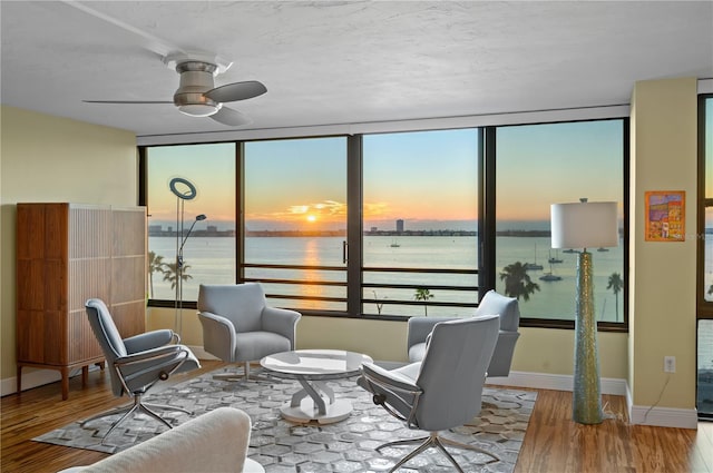 sitting room with a water view, light hardwood / wood-style flooring, and ceiling fan