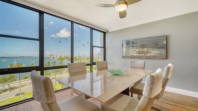 dining space with ceiling fan, floor to ceiling windows, a water view, and light hardwood / wood-style floors