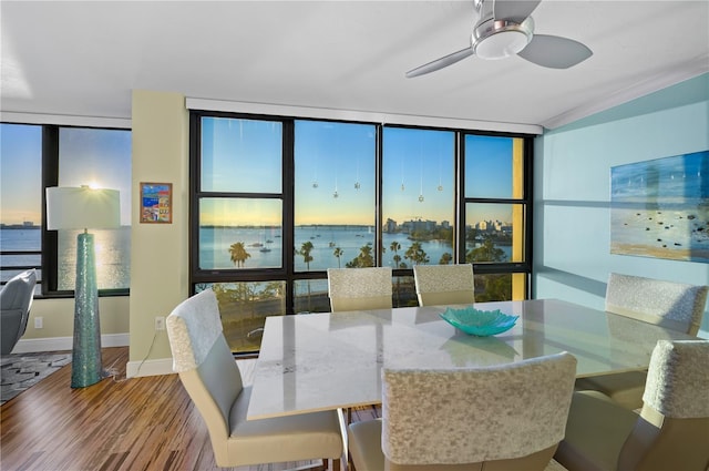 dining space featuring ceiling fan, a wealth of natural light, a wall of windows, a water view, and hardwood / wood-style flooring