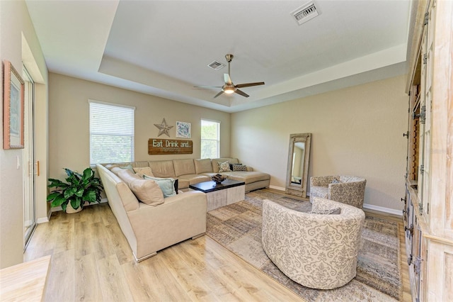 living room featuring ceiling fan, a raised ceiling, and light hardwood / wood-style flooring