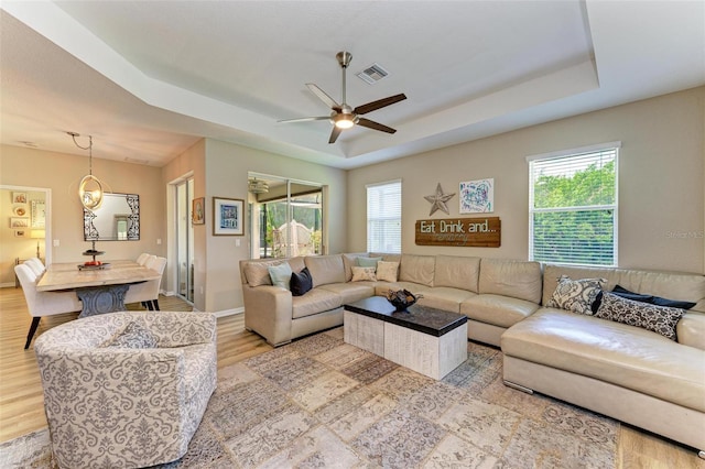 living room with a tray ceiling, light hardwood / wood-style flooring, a wealth of natural light, and ceiling fan