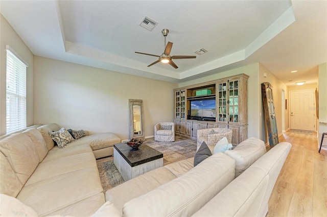 living room featuring a raised ceiling, ceiling fan, and light hardwood / wood-style flooring