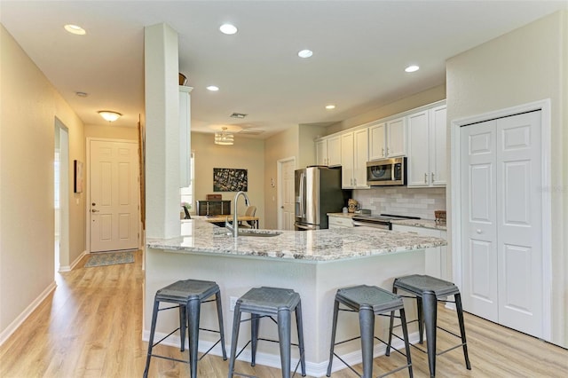 kitchen featuring kitchen peninsula, light wood-type flooring, stainless steel appliances, sink, and white cabinets